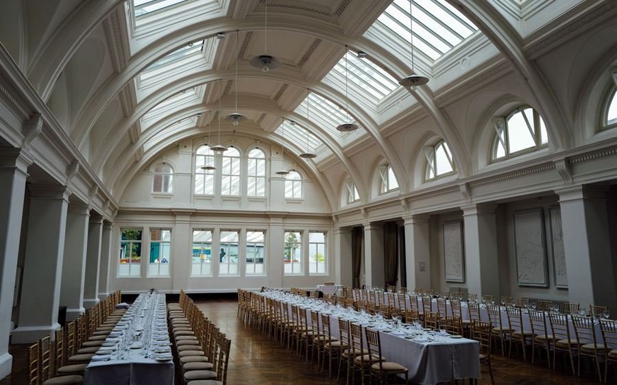Salón de banquetes con techo de cristal y mesas largas vestidas de blanco