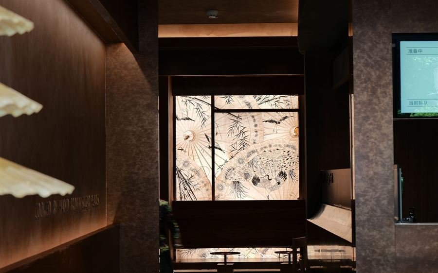 Interior de restaurante en penumbra con luz cálida y biombo iluminado al fondo